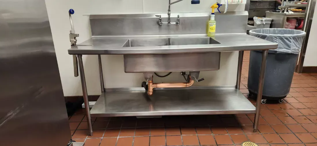 Stainless prep table and sink scrubbed down in a commercial kitchen