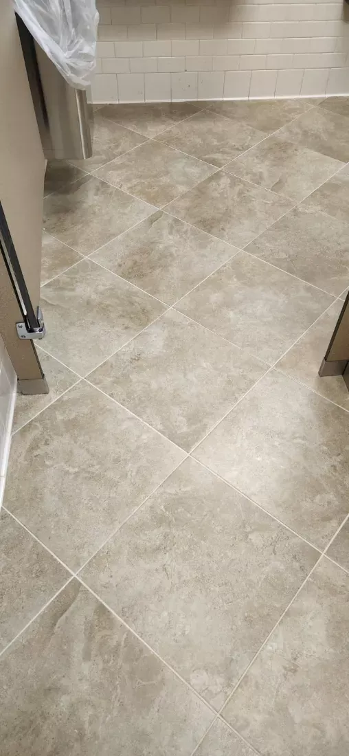 Travertine-look restroom floor cleaned along the stall partitions