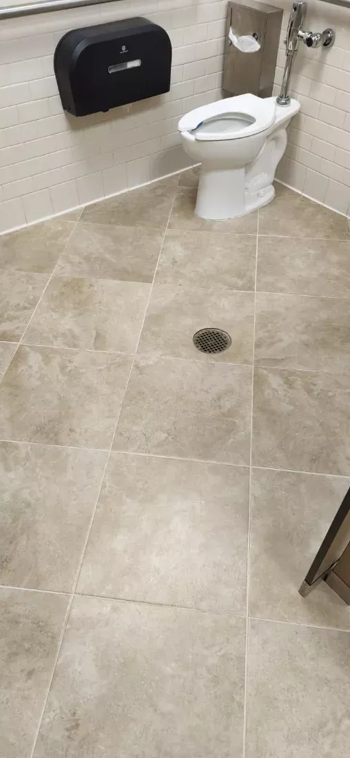 Large-format restroom tile floor mopped around the toilet and floor drain